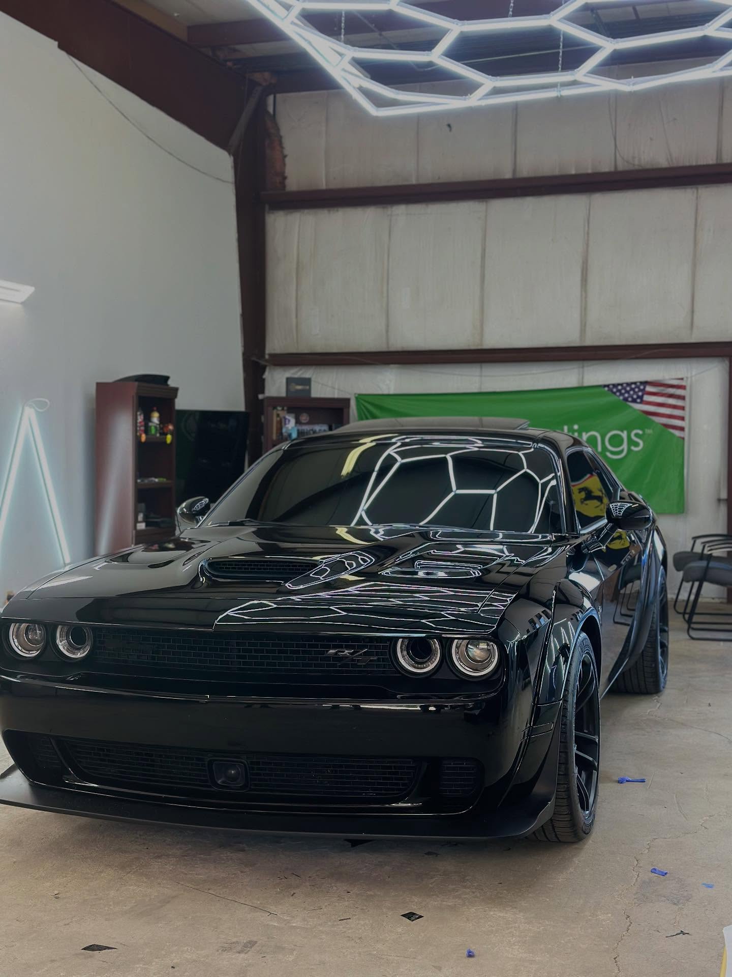 Black Dodge Challenger R/T with the shop's hexagon lights reflected in its glossy paint
