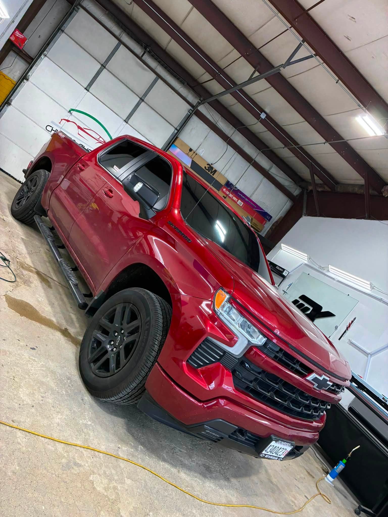 Red Chevrolet Silverado pickup with tinted windows and black wheels in the shop bay
