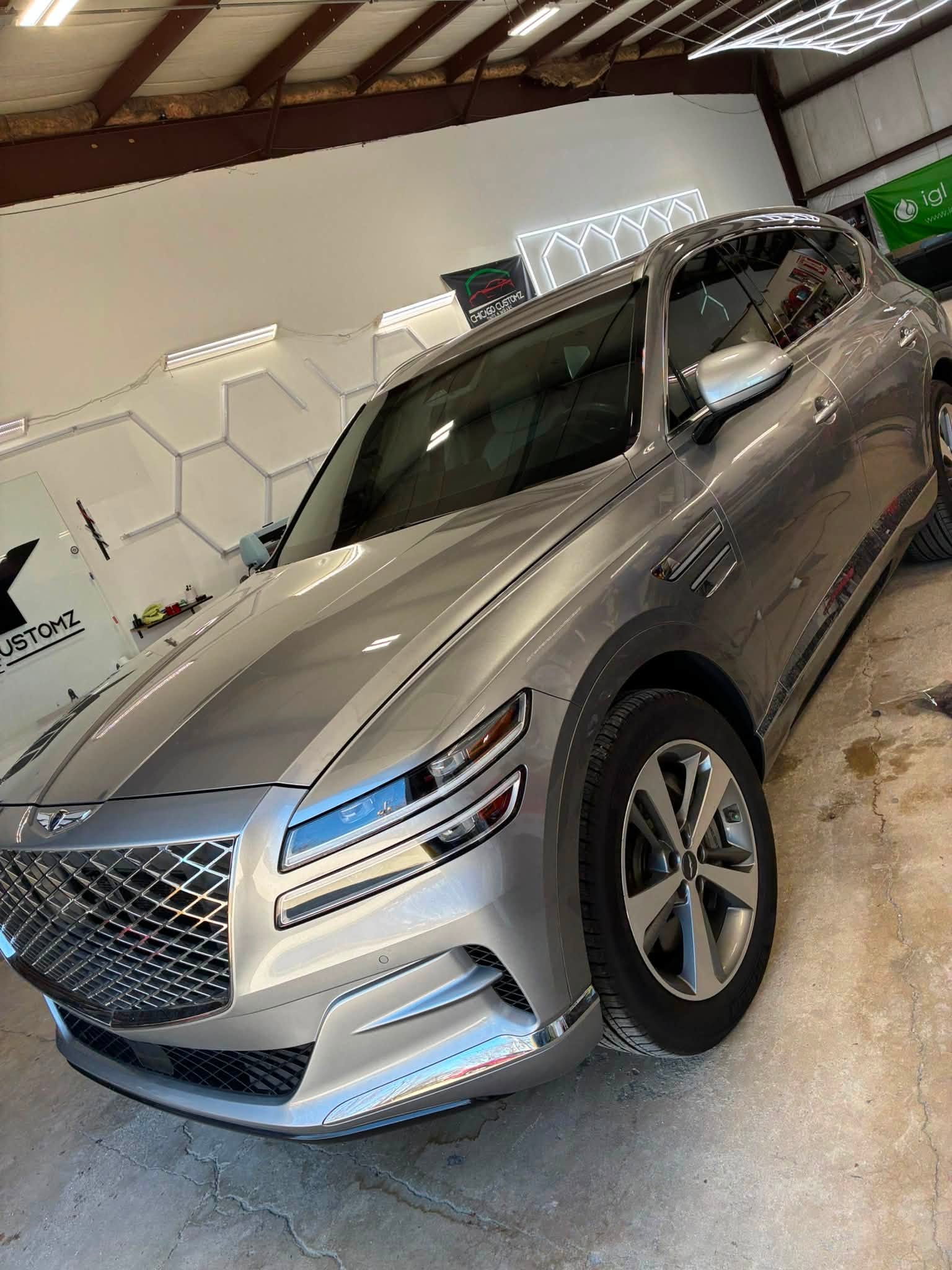 Silver Genesis GV80 SUV parked under the shop's hexagon LED light panel