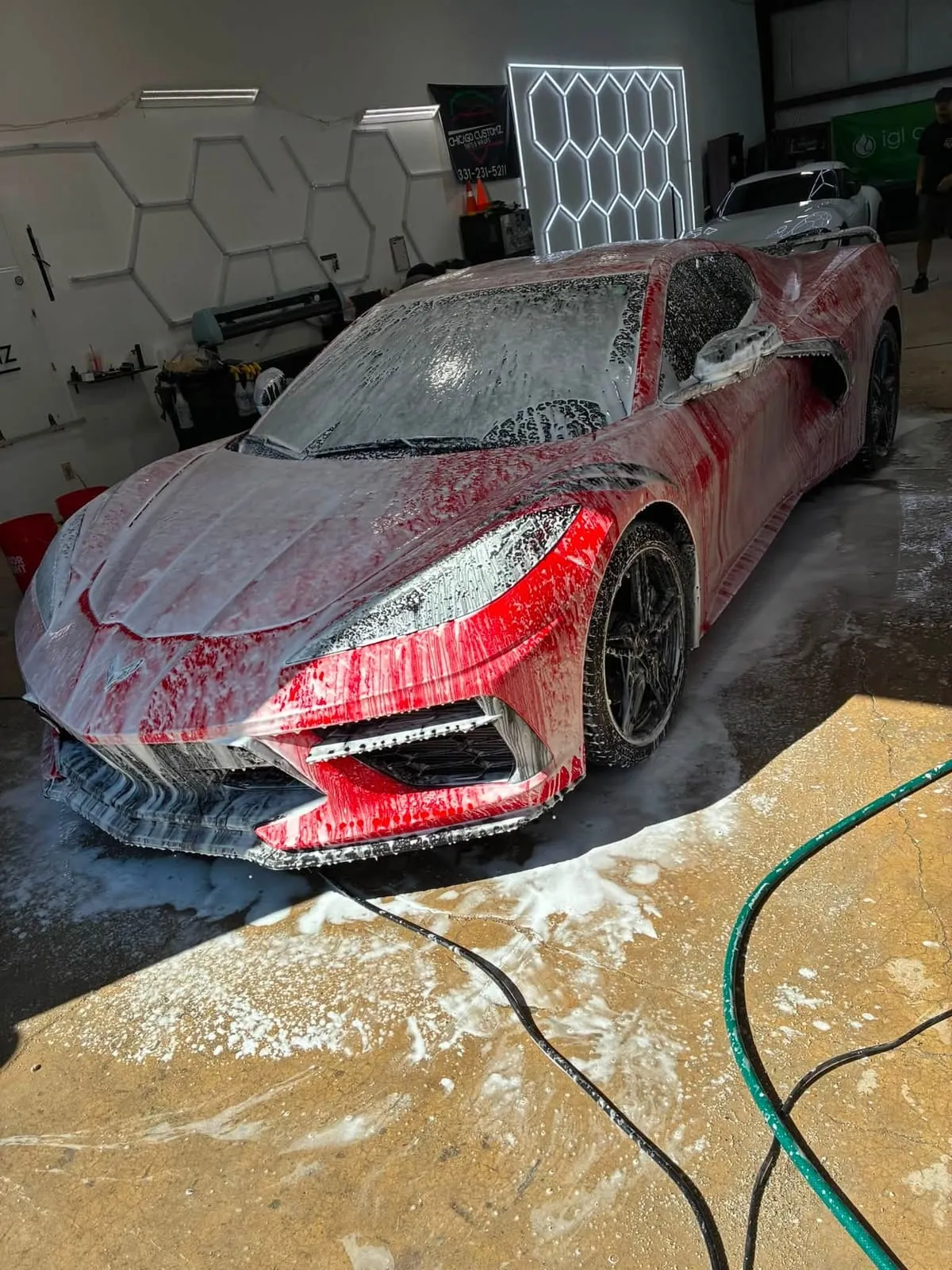 Red Chevrolet Corvette C8 covered in foam during a wash in the Prime Auto Lab bay